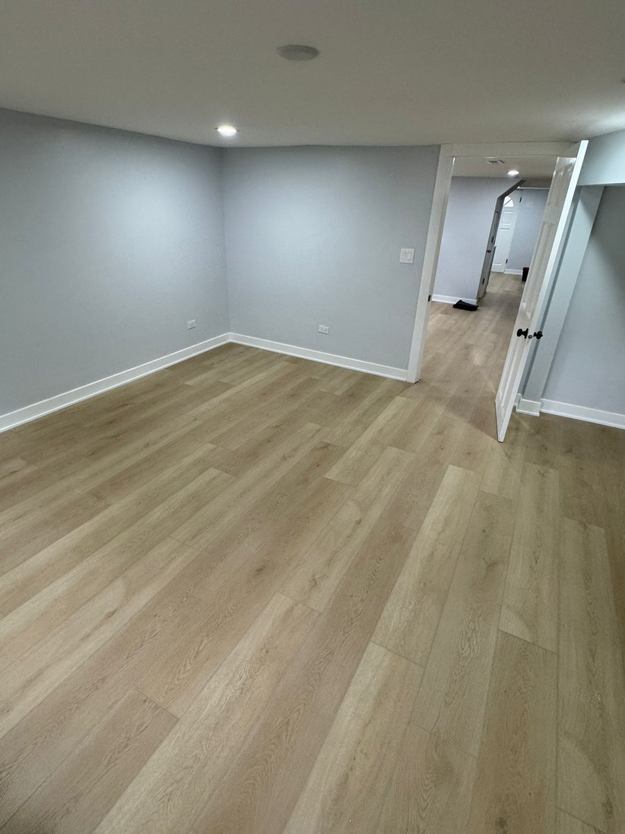 A finished lower-level bedroom in a light oak plank, laid over a levelled concrete slab.