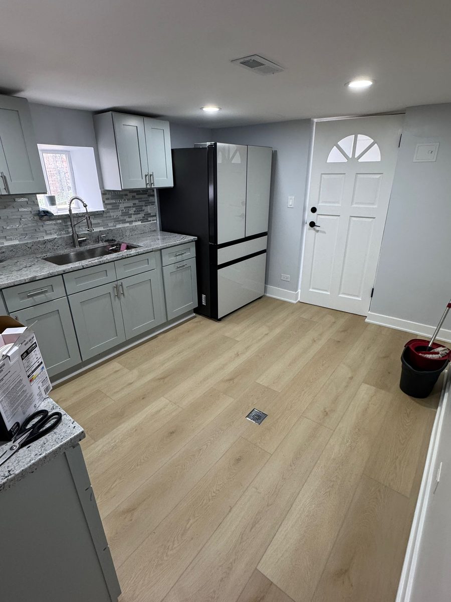 Kitchen floor in a pale oak plank, cut in around cabinet toe kicks and the exterior door threshold.